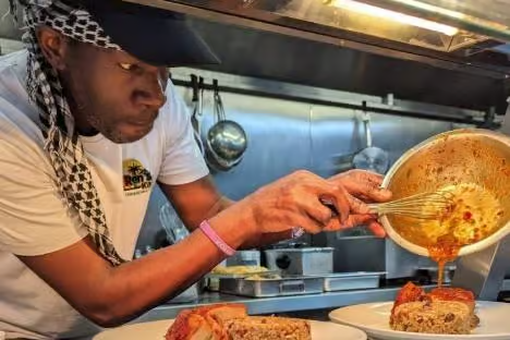 Chef Renoll Webb finishing a plate of Caribbean food with sauce in the Ren's Kitchen kitchen